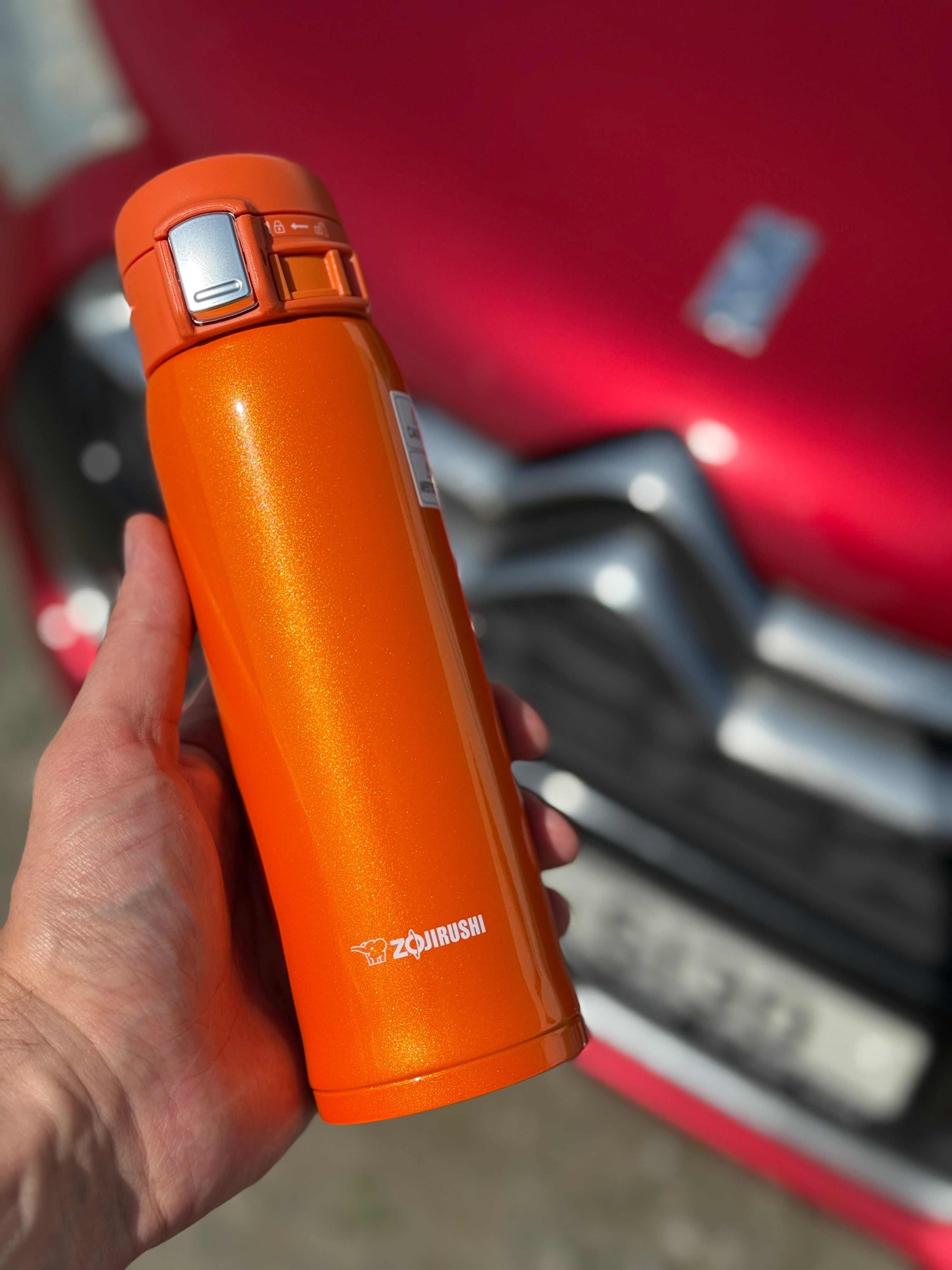 Person drinking from Zojirushi SM-SHE orange thermal mug, comfortable and ergonomic design