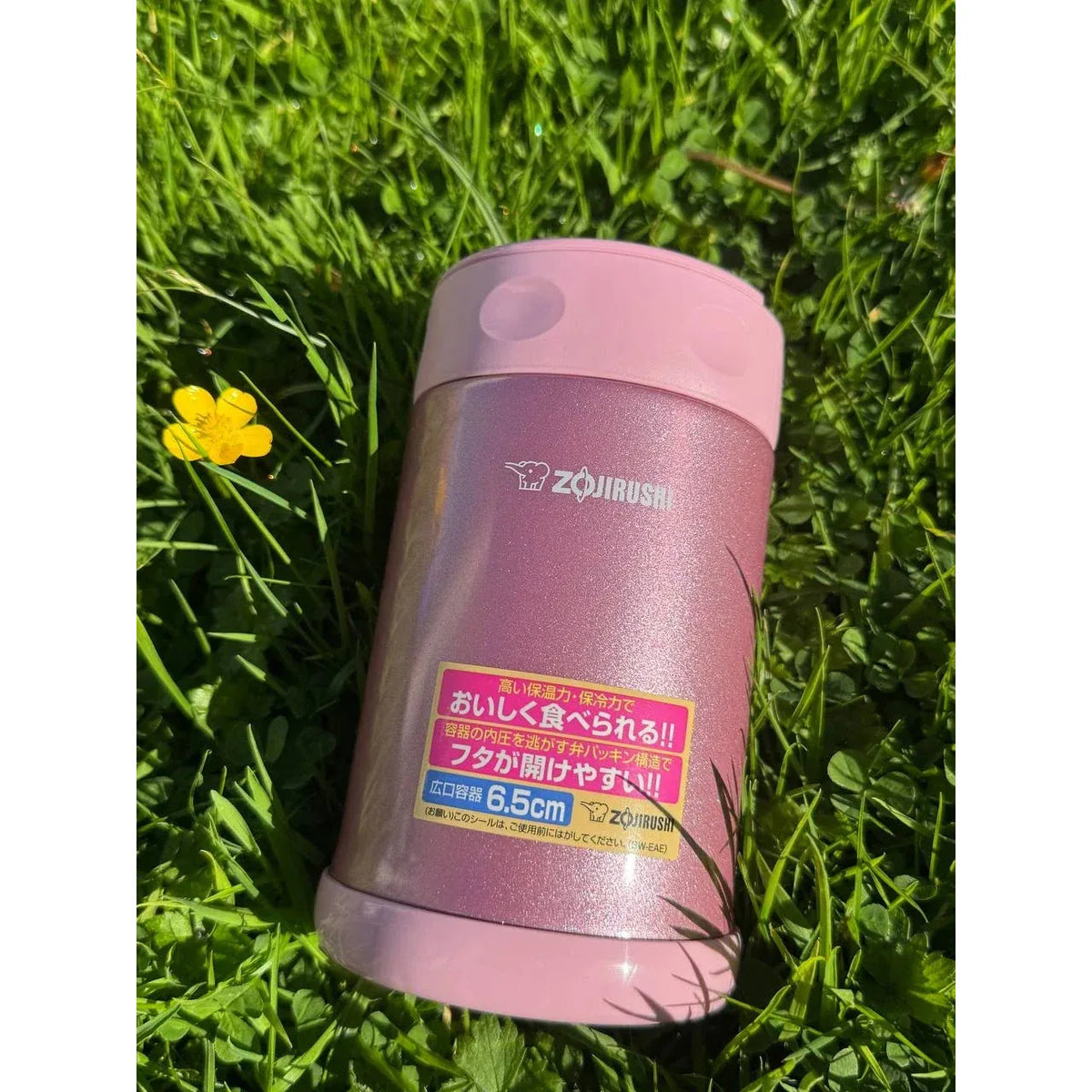 Zojirushi SW-EAE Pink 500 ml (16.9 oz) thermal food jar, stainless steel insulated lunch container photographed outdoors on green grass with a yellow flower.