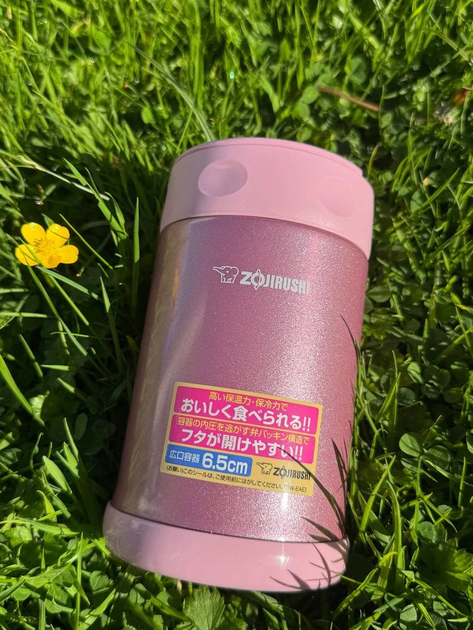 Zojirushi SW-EAE Pink 500 ml (16.9 oz) thermal food jar, stainless steel insulated lunch container photographed outdoors on green grass with a yellow flower.